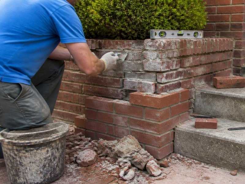 Brickmason rebuilding a damaged brick porch wing wall beside exterior steps in Madison, Alabama.