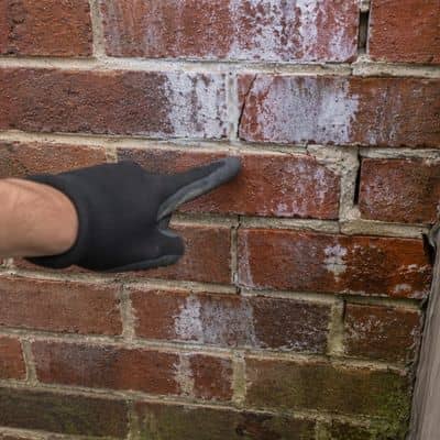 Close-up of a brick wall showing white stains, cracked mortar, and moisture damage being inspected after heavy rain