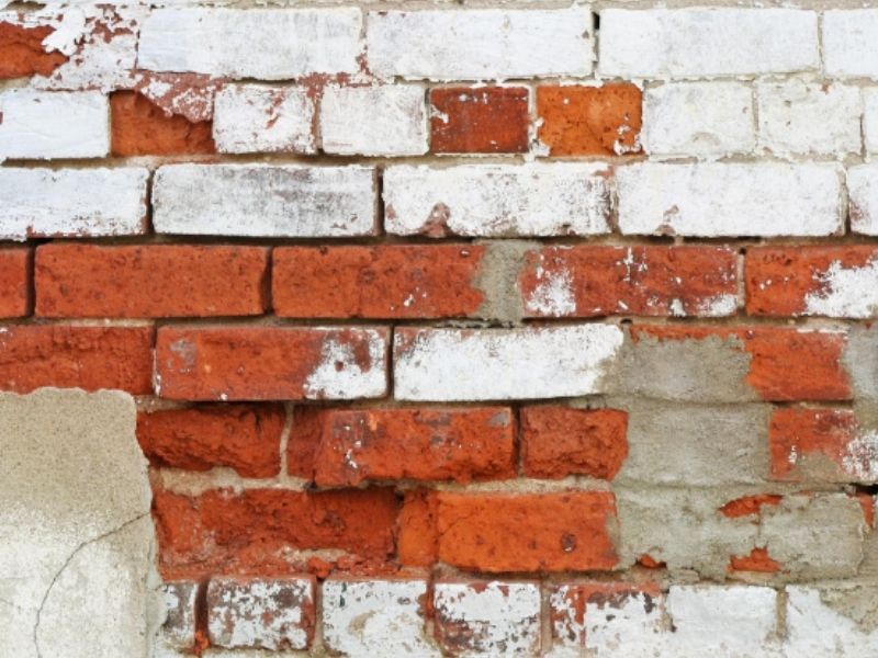 Painted brick showing peeling paint and moisture damage on a masonry wall