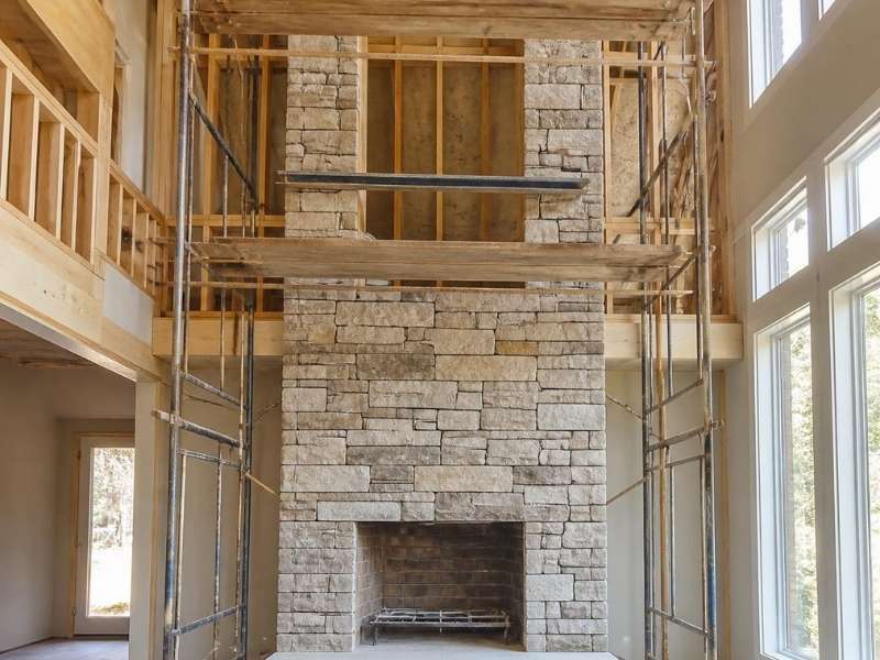 Two-story stone fireplace installation with scaffolding in a Madison, Alabama home.